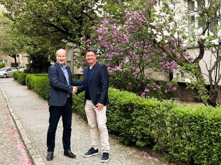 Zwei Herren geben sich die Hand und sehen in die Kamera
